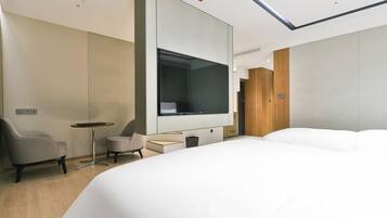 A modern hotel room with a large bed, a small desk, a chair, a TV, and a wardrobe.