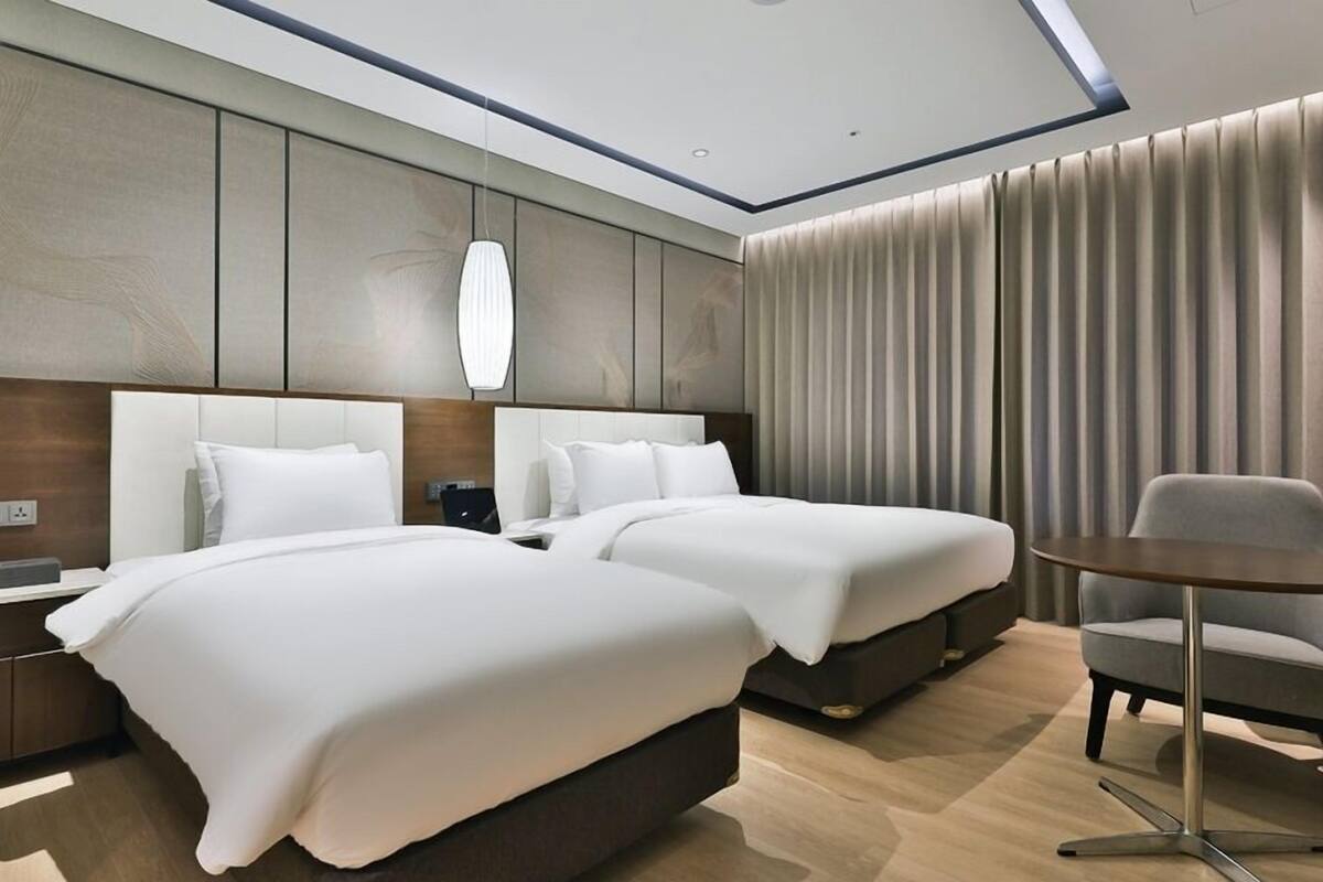Une chambre d’hôtel avec deux lits, un bureau, une chaise et une grande fenêtre avec des rideaux.