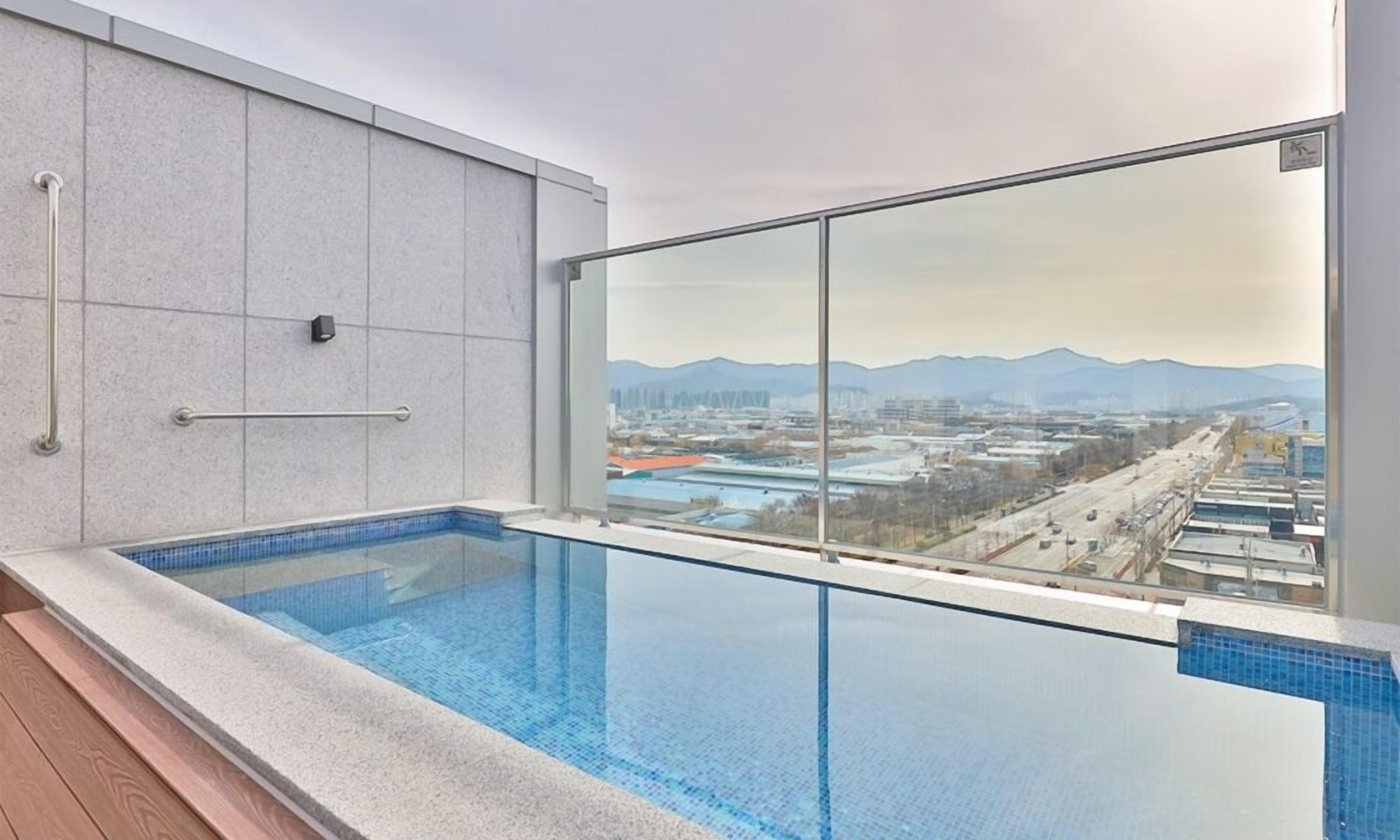 Una piscina interior moderna con vistas a la ciudad, un panel de vidrio y una barandilla de metal.