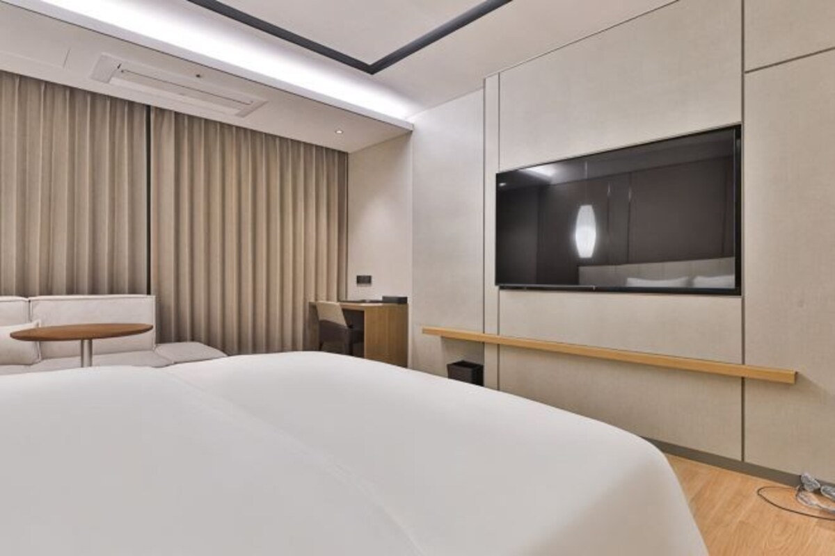 Una habitación de hotel moderna con una cama grande, un escritorio, una silla, un sofá y un televisor montado en la pared.