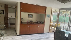 Una cucina moderna con un mobiletto in legno, un'area pranzo con un tavolo in vetro e vista all'esterno tramite ampie finestre.