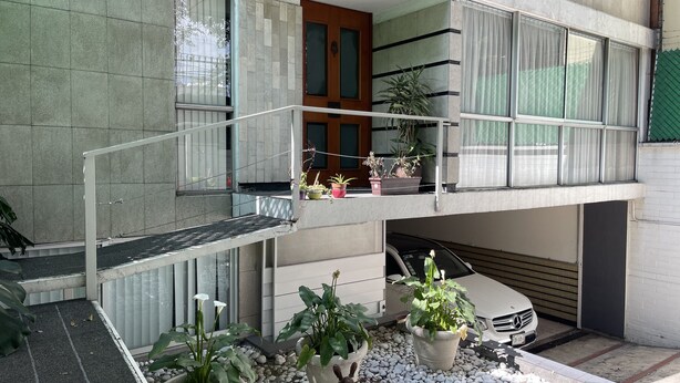 Un edificio residenziale a più piani con un balcone, piante in vaso e un’auto parcheggiata.