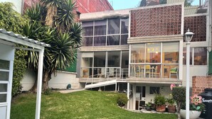 Un edificio su due piani con un balcone, un piccolo giardino e una recinzione bianca.