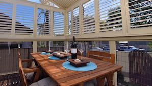 A covered patio with a wooden table set for dining, featuring a bottle of wine and glasses. - Point Bulli (Bulli)