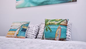 A bed with three pillows, each featuring a different beach scene. - Point Bulli (Bulli)