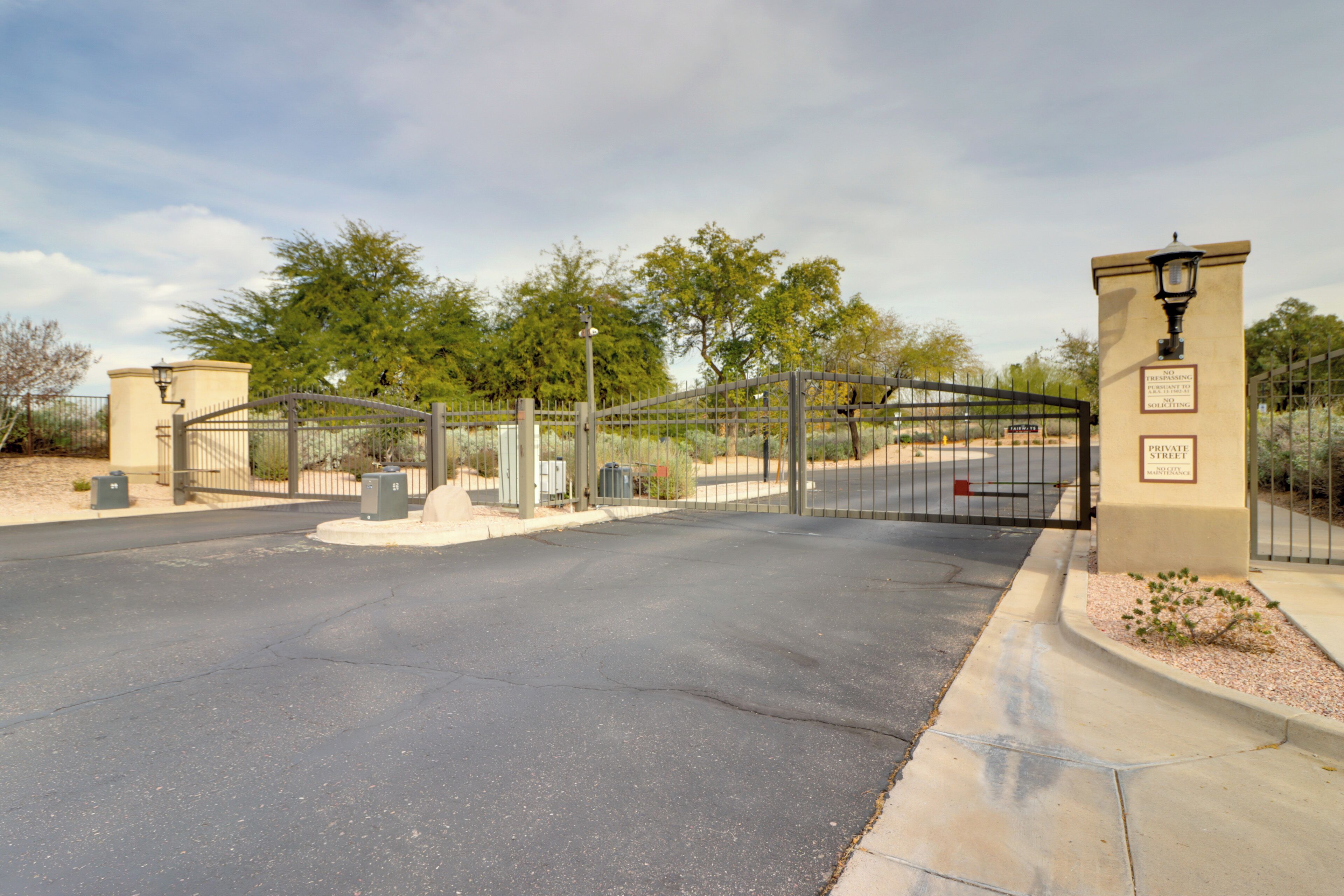 A gated entrance with a metal fence, a street sign, and a lamp post.