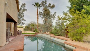 Une piscine avec un espace patio, entourée d’arbres et d’une clôture.