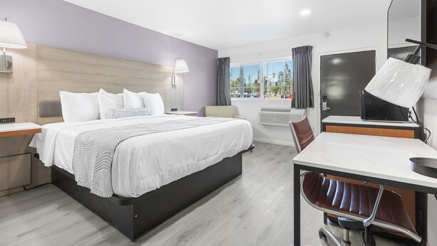 A modern hotel room with a large bed, a desk, and a chair. -  Inland Inn & Suites (San Bernardino)