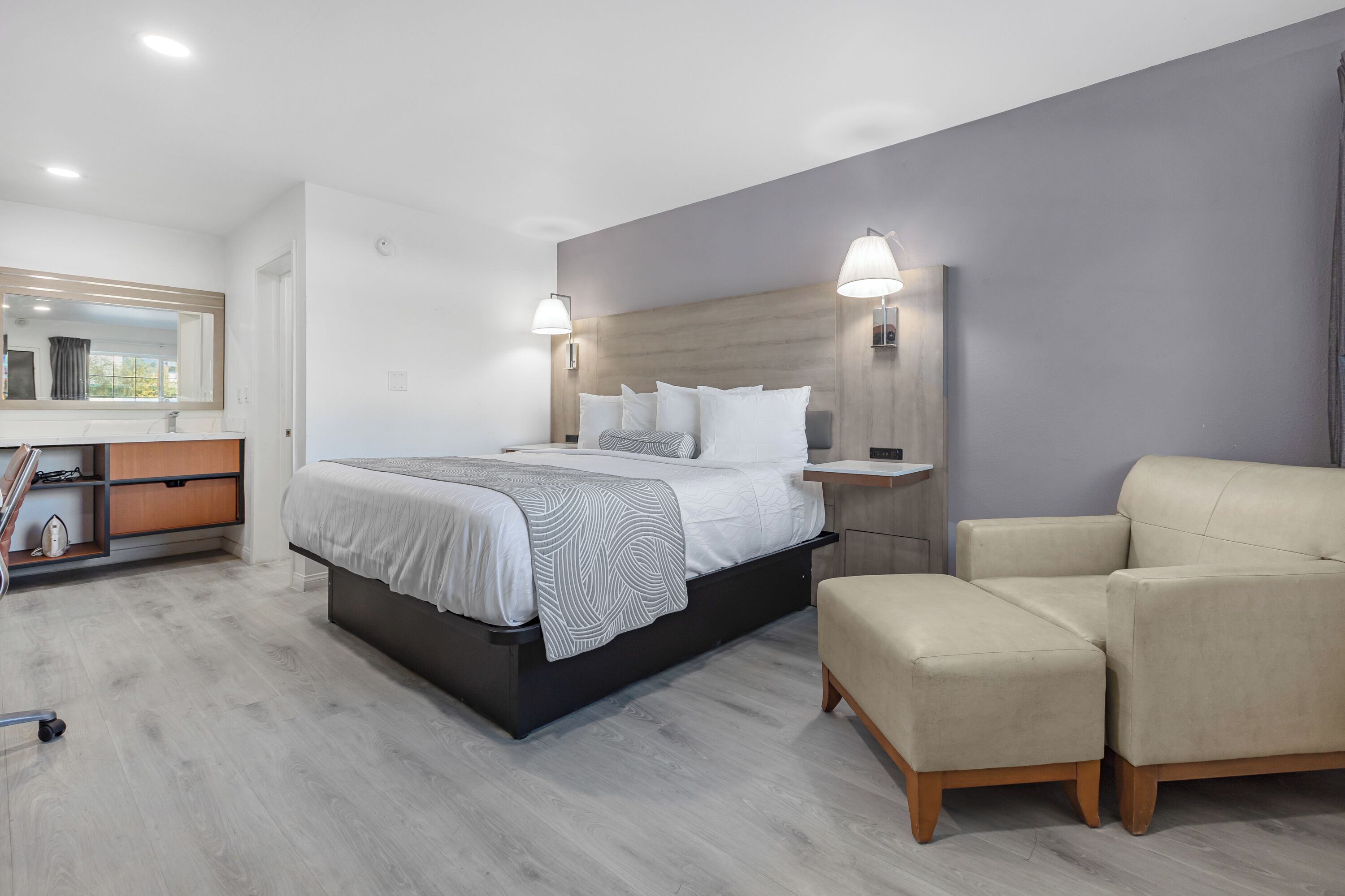 Una habitación de hotel moderna con una cama grande, lámparas de noche, un sofá y una mesita de noche de madera.