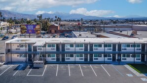 A multi-story hotel with a parking lot, a billboard advertising a restaurant, and a mountainous backdrop. -  Inland Inn & Suites (San Bernardino)