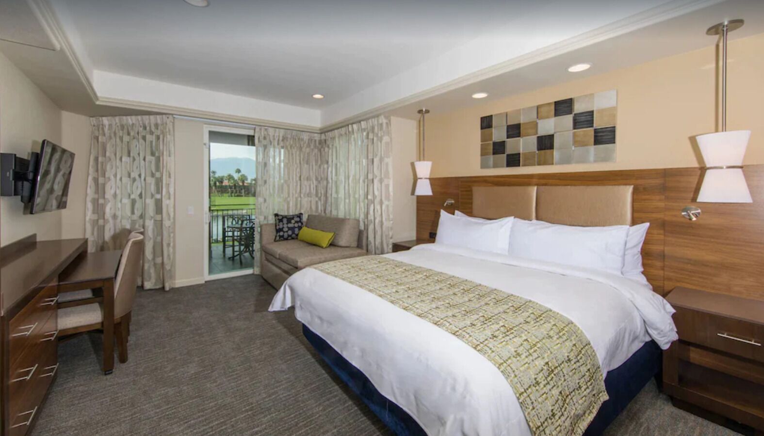 Une chambre d’hôtel avec un grand lit, un bureau, une chaise, un canapé et un balcon avec vue.