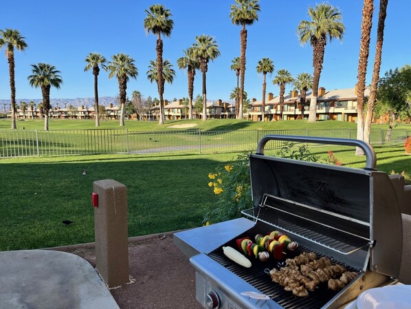 A barbecue grill with skewers of vegetables and meat, set against a backdrop of a golf course and palm trees. - Marriott Desert Springs Villas II-Spacious 1 Bdr Full Resort Access (Palm Desert)