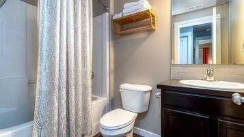 A bathroom with a shower curtain, toilet, and vanity with a mirror.