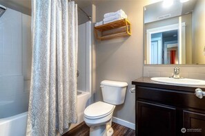 Et badeværelse med bruseforhæng, toilet og vaskebord med spejl.