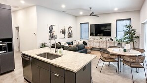 A modern kitchen with a central island, a dining area with a round table and chairs, and a living room with a sofa and a TV. - City Escape near Sarasota Downtown (Sarasota)