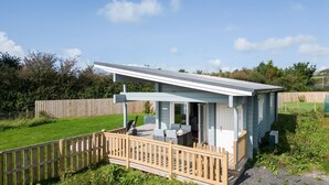 Een klein, lichtblauw houten gebouw met een overdekt terras, een omheind terras en een gazon.