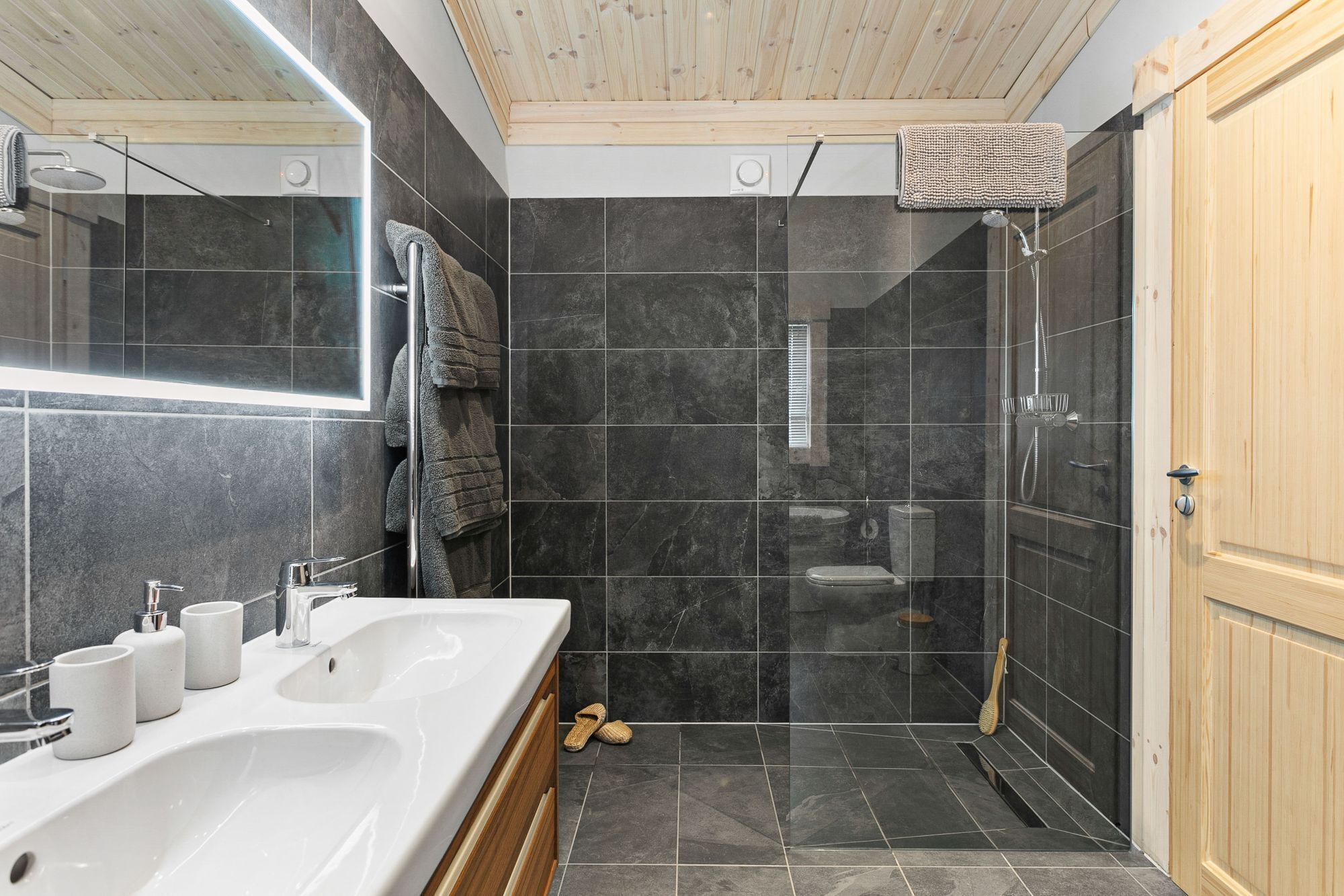 A modern bathroom with a large white bathtub, a shower enclosure, and a wooden door.