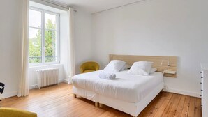 A bedroom with a large window, a wooden floor, a bed with white bedding, and a yellow chair. - Charming town house completely renovated (Quimper)