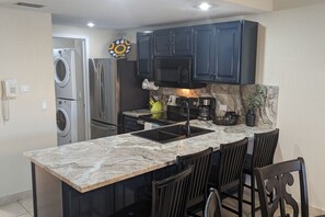 A kitchen with dark cabinets, a marble countertop, a built-in microwave, and a coffee maker. - Ocean Front Resort 2-Bedroom Condo at Princesa de Peñasco with Amenities (Puerto PeÃ±asco)