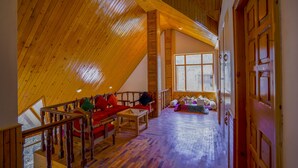 A spacious loft with a high ceiling, wooden beams, a cozy seating area with a sofa and chairs, and a large window providing natural light.