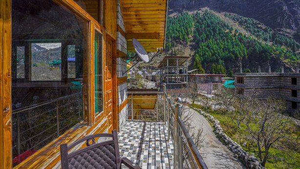 A wooden balcony with a tiled floor, a chair, and a view of a mountainous landscape with buildings.