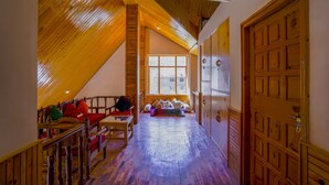 A cozy attic room with a sloped wooden ceiling, a large window, and a wooden door.