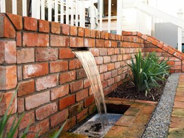 Pared de tijolos com uma pequena cascata e um vaso com folhagem verde.