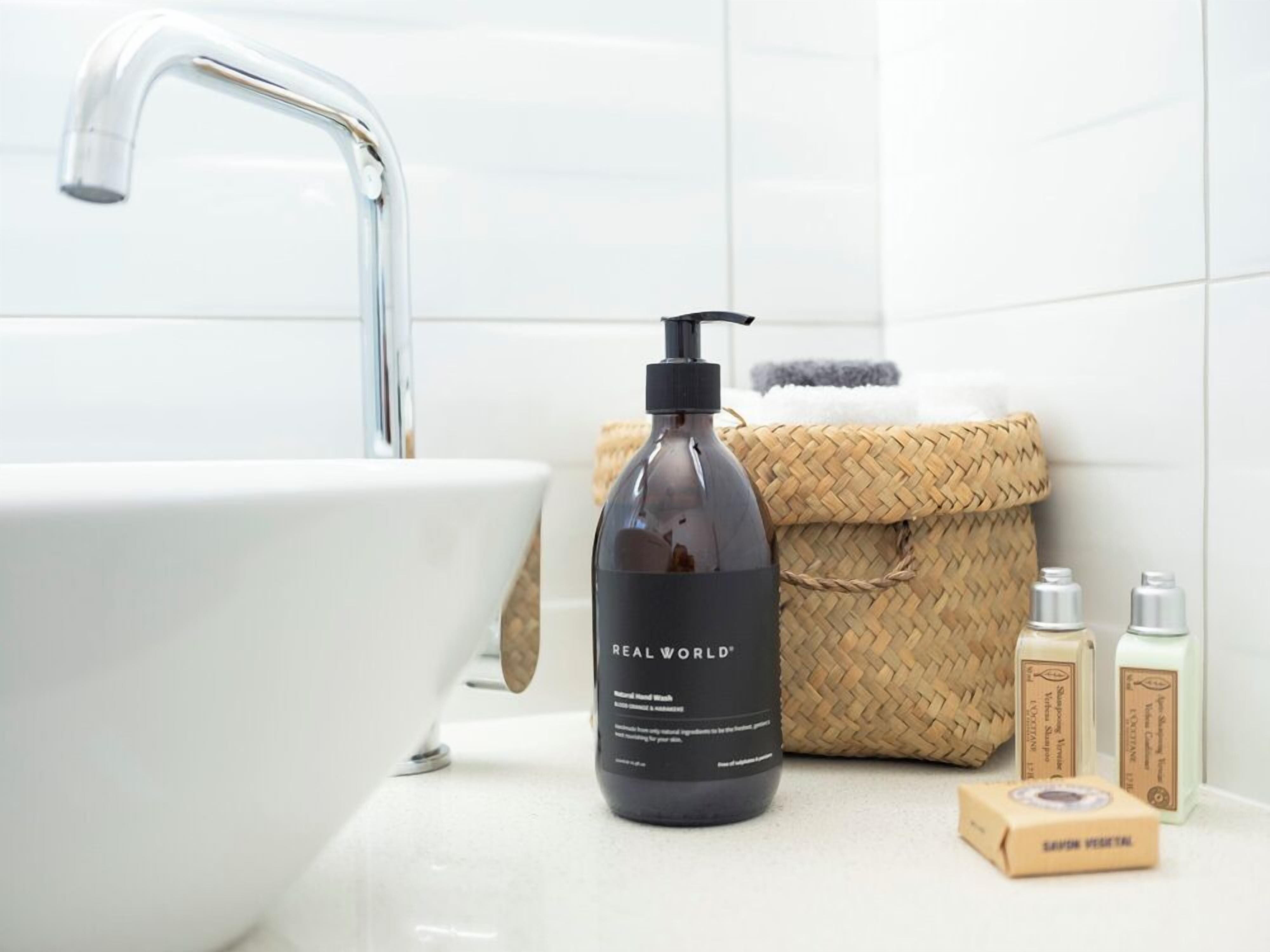 A bathroom with a white sink, a black bottle of Real World shampoo, and two soap bars.