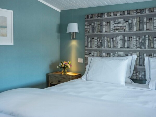 Un dormitorio con una cama, una mesita de noche con lámpara, un jarrón de flores y una pared con diseño de estantería.