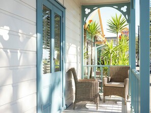 A porch with wicker furniture, a door, and potted plants. - 415 Marine Parade (Napier)