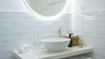 Un baño moderno con un lavamanos blanco, espejo redondo y paredes con azulejos.
