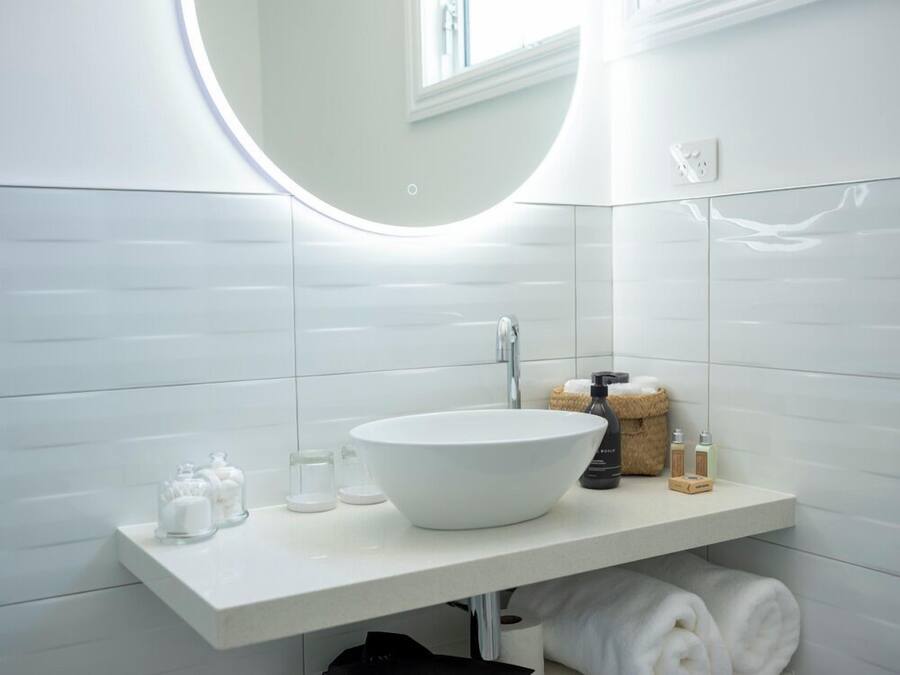 Un baño moderno con un lavamanos blanco, espejo redondo y paredes con azulejos.