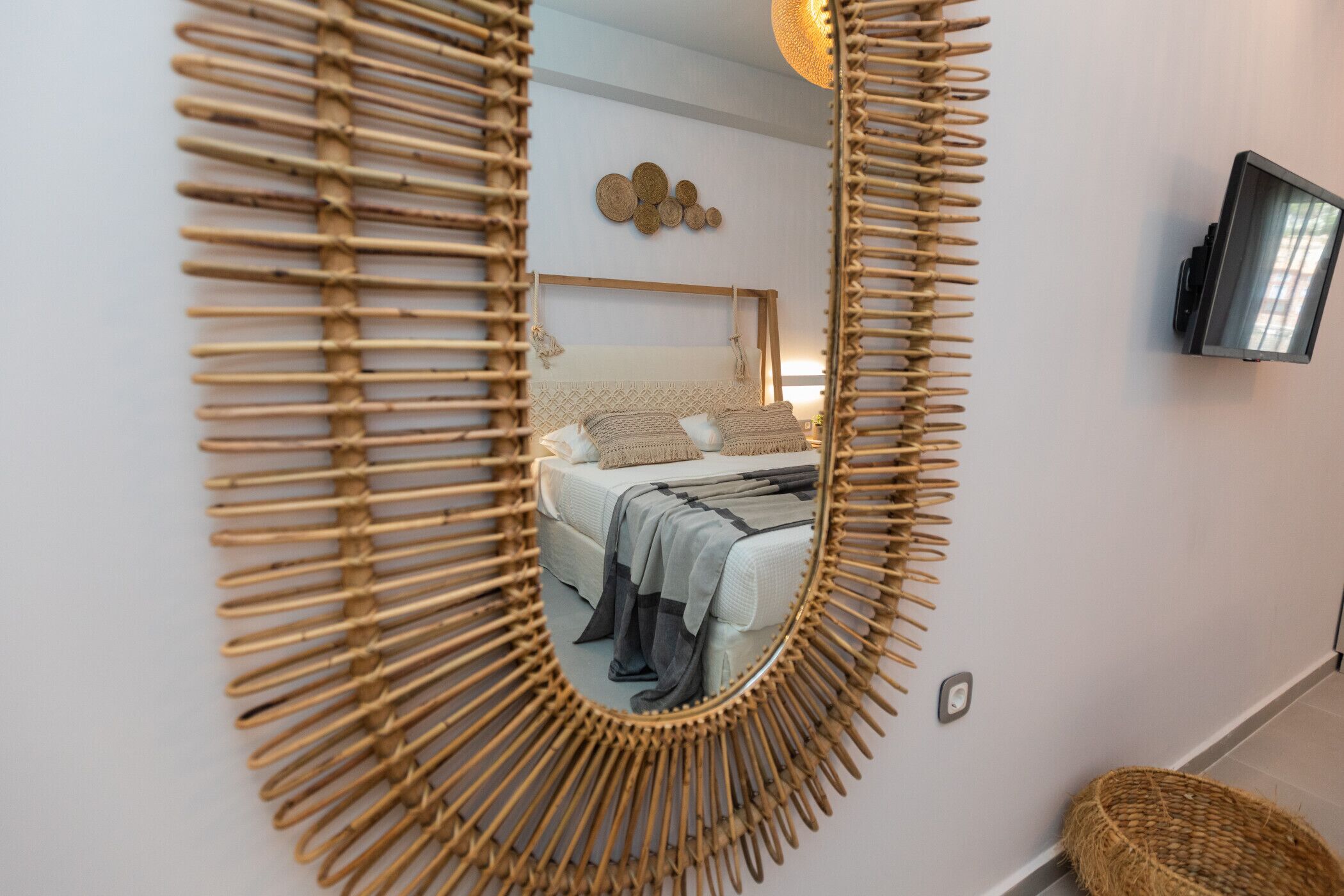 Una habitación con un espejo grande, una cama con cabecera, un televisor montado en la pared y una cesta tejida.
