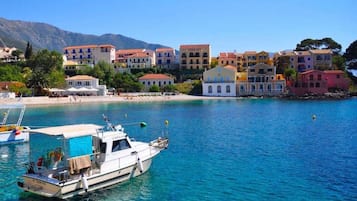 Une ville côtière aux bâtiments aux couleurs vives, bordée d’une mer d’un bleu limpide, où des bateaux sont amarrés dans le port.