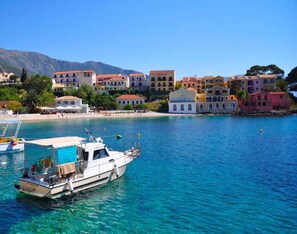 Un pueblo costero con edificios de colores, un mar azul cristalino y barcos amarrados en el puerto.