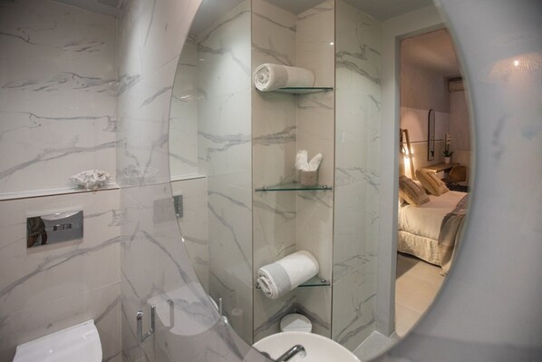 Un baño moderno con pared de mármol, cabina de ducha de vidrio, inodoro y lavamanos.
