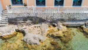 Un muro de piedra con aberturas en arco, una barandilla blanca y agua cristalina en la base.