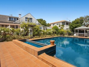 Piscina com deck revestido, cercada por um jardim com diversas plantas e um gazebo.
