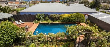 Quintal residencial com piscina, cercado por um muro e diversas plantas.