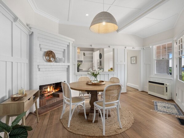 A dining area with a round wooden table, white chairs, a woven rug, and a fireplace. - Roma in the Heart Mornington (Mornington)