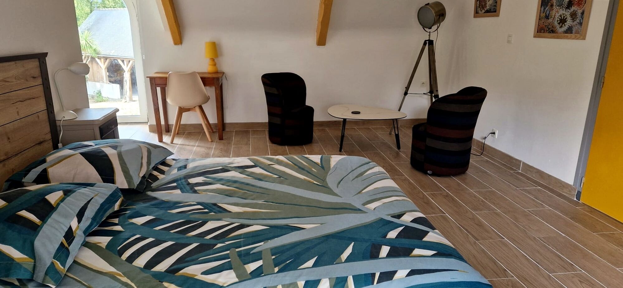 Een slaapkamer met een bed, een bureau, een stoel, een lamp en een staande lamp.