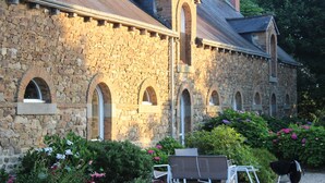 A stone building with arched windows and a wooden deck with outdoor furniture. - Les Cavaliers, character gîte with swimming pool, 20 minutes from the seaside (La Poterie, Lamballe)