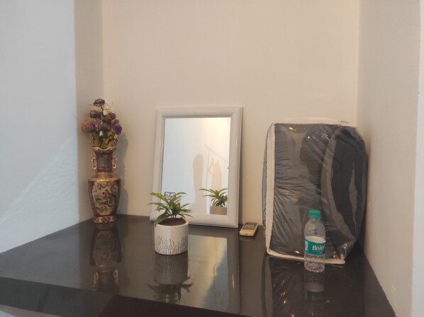 Una mesa con un jarrón de flores, un cuadro enmarcado, una planta en maceta, un objeto envuelto y una botella de agua.