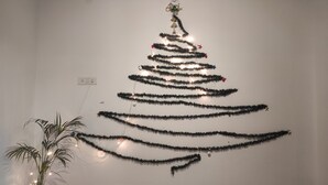 A wall-mounted Christmas tree made of tinsel and lights, with a star ornament at the top. - Homocation The Corporates Homestay (Guwahati)