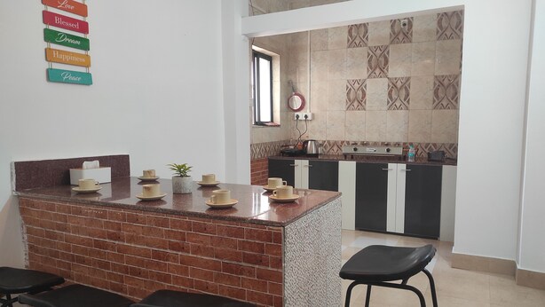 A kitchen with a brick island, black stools, and a tiled backsplash. - Homocation The Corporates Homestay (Guwahati)