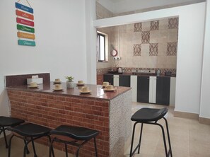 A kitchen with a brick island, black stools, and a tiled backsplash. - Homocation The Corporates Homestay (Guwahati)