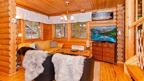 A cozy log cabin interior with a sofa, a television, a wooden cabinet, and a fireplace.