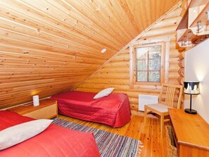 A cozy cabin with two beds, a small table, a chair, a heater, and a window with blinds.