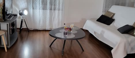 A living room with a round coffee table, a sofa, a TV on a stand, and a painting on the wall.