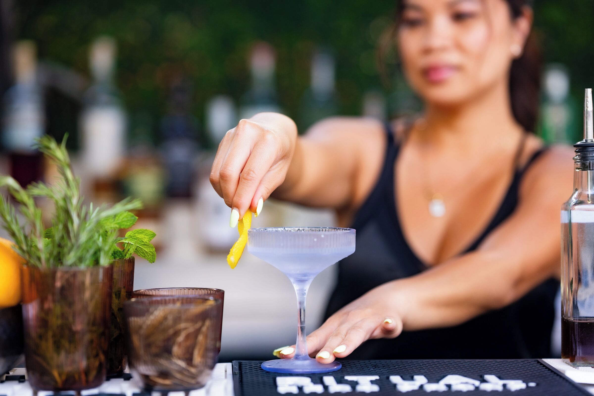 A person preparing a drink with a bar spoon and a martini glass on a table with a keyboard and a bottle.